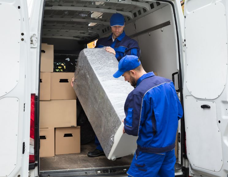 Två transportörer lastar en skyddad möbel i en vit flyttbil.